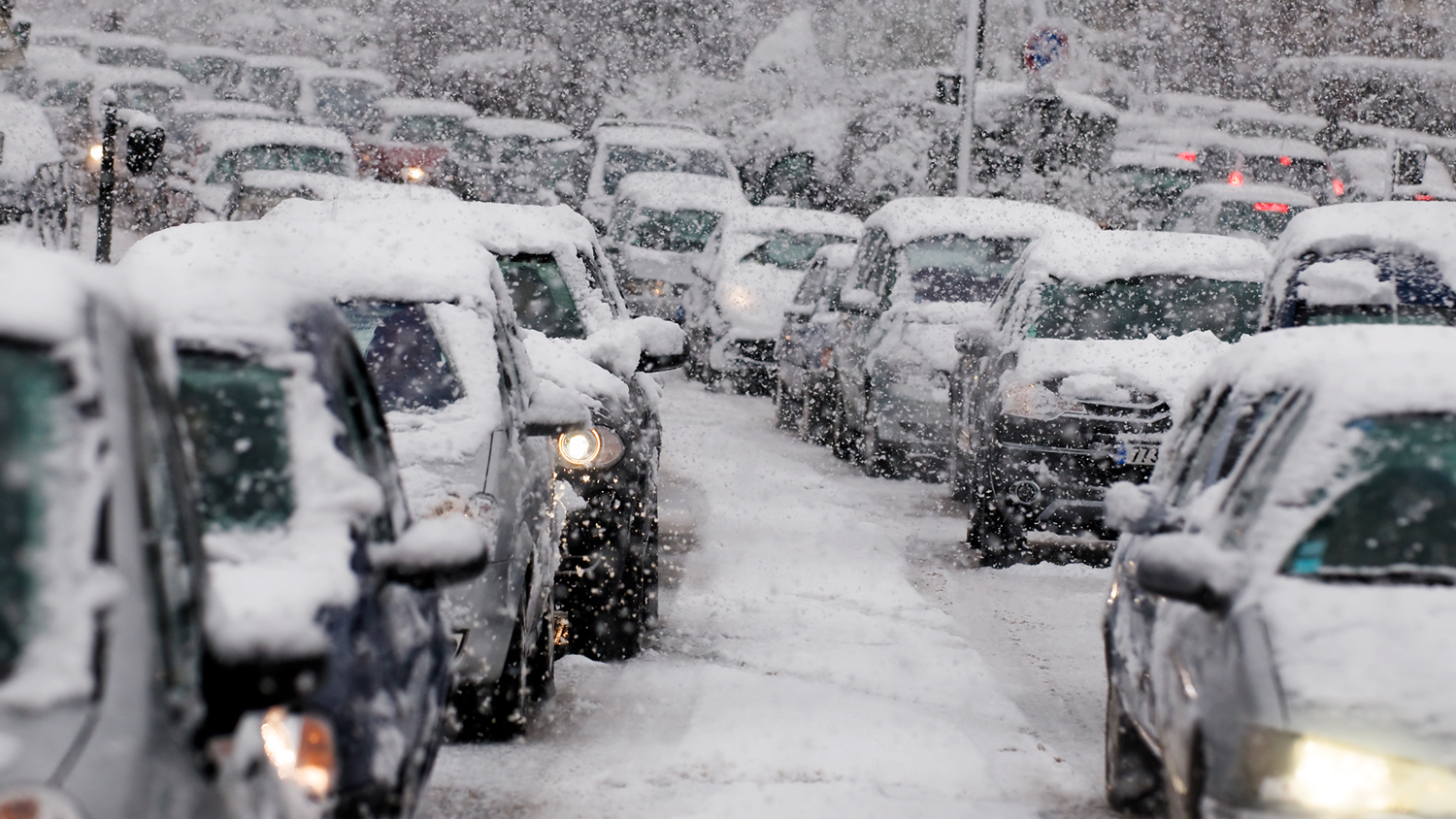 Rijen auto's, bedekt met sneeuw, wachten op besneeuwde wegen.